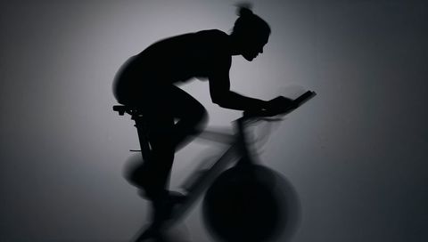 Pedaling cyclist leaning forward on indoor trainer silhouette backlit spinning motion