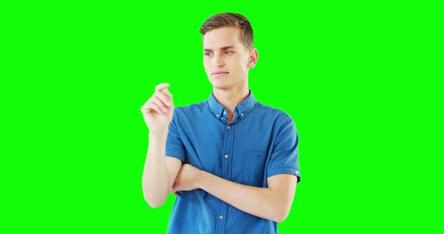Young man in blue shirt contemplating while pointing, with arms crossed, isolated on green screen background. Perfect for ads, presentations, educational videos, and graphic design where you want to overlay content on a versatile green screen background.