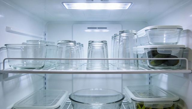 Minimalist fridge interior showing clear glassware glinting under led light with avocados