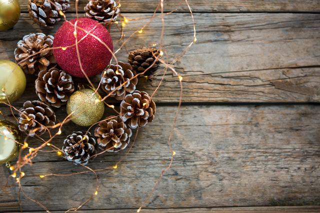 Close-up of rice lights, bauble ball and pine cone on wooden plank during christmas time