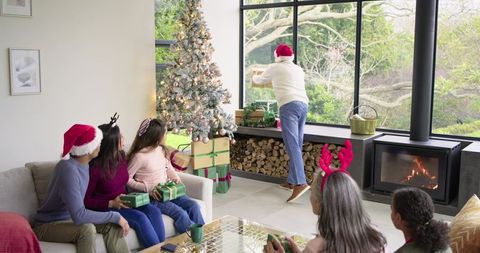 Diverse family celebrating christmas, holding gifts and watching surprise outside window