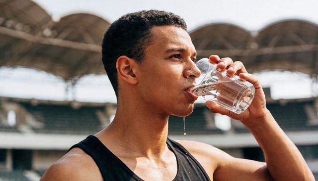 Male Athlete Drinking Water During Outdoor Stadium Training Showing Post-Workout Hydration