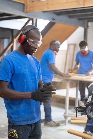 African american carpenters working in woodshop wearing safety gear and shaping planks