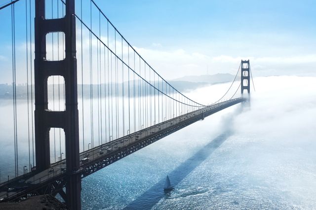 Golden Gate Bridge emerging through thick morning fog in San Francisco Bay. Ideal for travel websites, posters, and articles showcasing iconic landmarks, architectural marvels, and scenic views of California. Perfect for backgrounds, nature themes, or engineering-focused content.