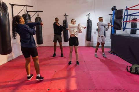 Diverse trainees stretching and warming up near boxing ring on red mats for group training