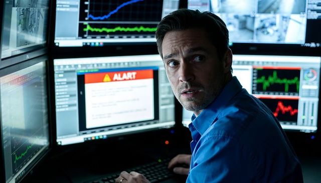 Cybersecurity analyst monitoring alert-filled multi-monitor dashboard in control room
