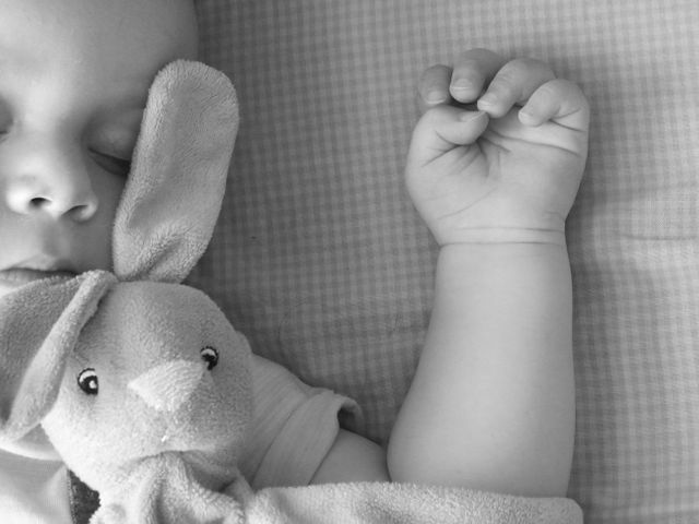 This heartwarming close-up photo shows a baby peacefully sleeping while cuddling a soft toy bunny. The focus is on the serene expression of the infant and the gentle grip on the bunny's ear. Perfect for use in parenting blogs, baby product advertisements, childcare promotions, or articles on infant sleep routines. The image conveys a sense of tranquility, comfort, and innocence, making it ideal for use in materials related to baby care and gentle parenting.