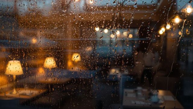 Raindrops on window overlooking cozy café interior at dusk with warm amber glow