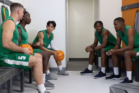 Basketball team discussing strategy in locker room wearing green uniforms showing camaraderie