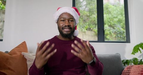 African American man wearing Santa hat speaking on couch in cozy Christmas livestream