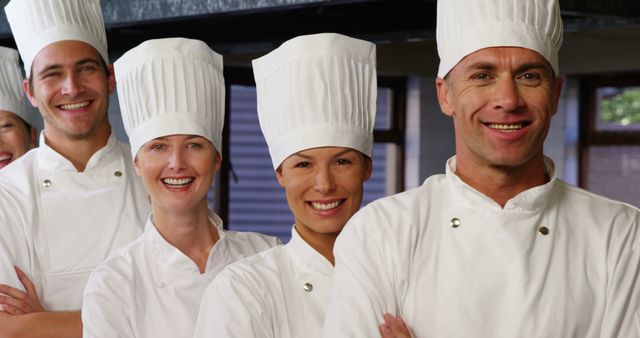 Group of smiling chefs in white uniforms and chef hats standing together in professional kitchen. Suitable for use in articles, blogs, or advertisements related to culinary arts, chef teamwork, restaurant promotions, and professional cooking environments.