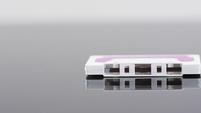 Retro cassette tape with pink label reflecting on grey surface signifies classic and nostalgic elements. Suitable for illustrating music history, vintage themes, and analog audio design.