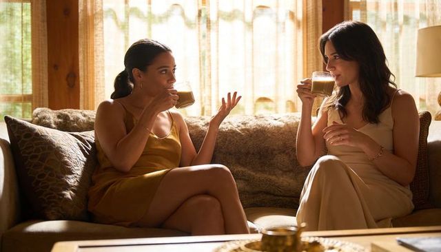 Two women chatting and sipping coffee on cozy sofa in warm living room ambience