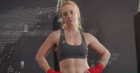Determined female boxer standing hands on hips in gym showing strength and focus