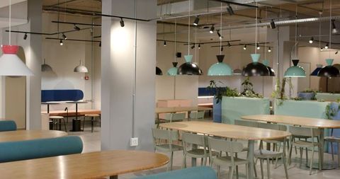 Modern pastel coworking cafeteria with wooden oval tables, green chairs and pendant lighting