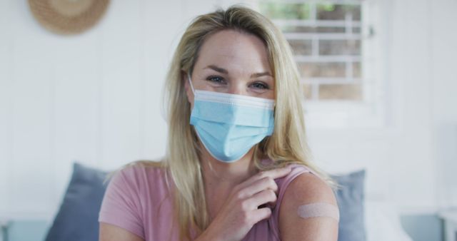 Woman wearing protective mask shows bandaged arm after getting vaccinated, smiling at camera. Ideal for campaigns promoting health awareness, vaccination drives, healthcare advertisements, and medical articles on COVID-19 prevention.