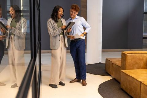 Diverse coworkers collaborating in modern office lounge reviewing tablet and documents