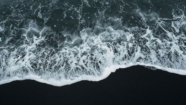 Aerial volcanic black sand coastline with crashing lace seafoam patterns
