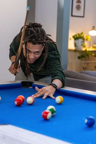 African american man aiming pool shot on blue-felt table in cozy home lounge