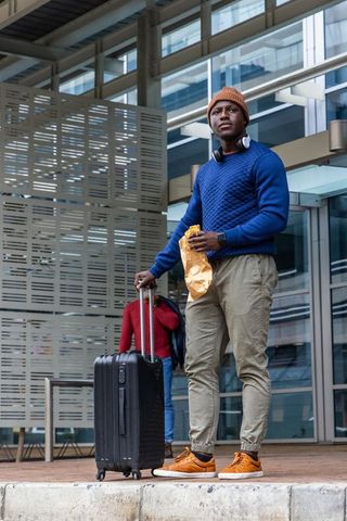 African american traveler standing with suitcase and snack at modern transit concourse