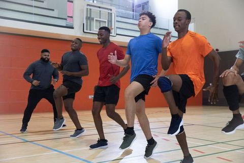 Diverse male athletes performing high-knee drill in indoor gymnasium for team training