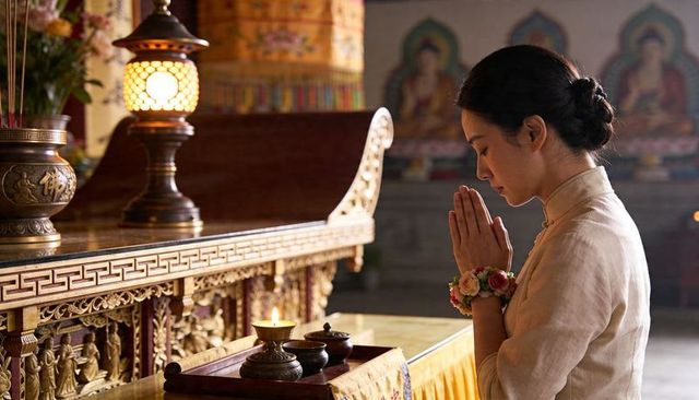 Praying asian woman kneeling at ornate temple altar, devotional ritual, warm candlelight