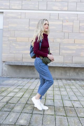 Young woman pausing with backpack and crossbody bag on urban plaza, casual street style
