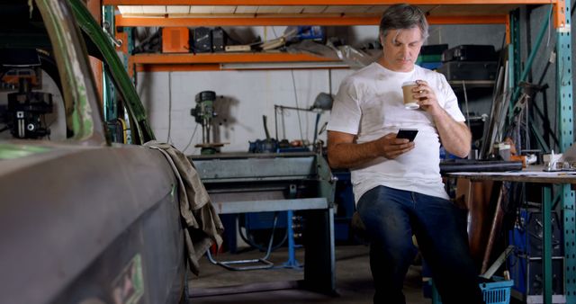 Mechanic Relaxing in Workshop Drinking Coffee and Using Smartphone - Download Free Stock Images Pikwizard.com