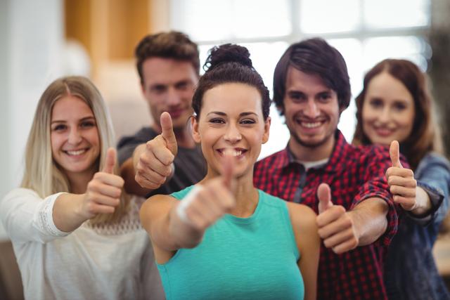 Group of young business professionals showing thumbs up, expressing positivity and teamwork in a modern office environment. Ideal for use in business presentations, team-building materials, motivational content, and corporate websites to convey success, unity, and a positive work atmosphere.