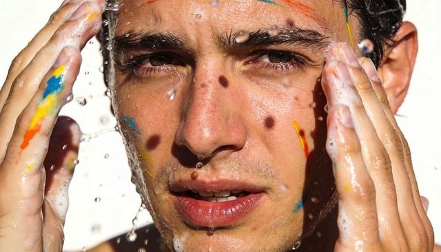 Splashing Hispanic Male Rinsing Face with Soap Foam and Paint Streaks Closeup Portrait