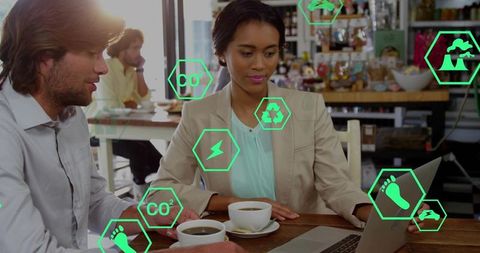 Professionals reviewing sustainability metrics at coffeehouse with laptop and green icons