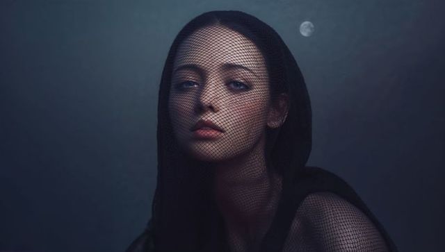 Veiled woman under moonlight wearing black mesh hood portrait evoking lunar mystery