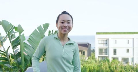 Smiling asian woman by coastal apartment with sea view and tropical foliage