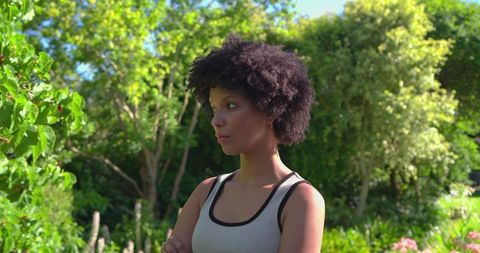 Confident african woman standing with arms crossed in sunlit lush garden portrait summer