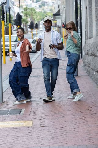 Multiracial friends walking down city sidewalk enjoying coffee, laughing, urban lifestyle