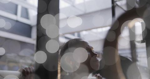 Young woman gazing up through modern atrium skylight while gripping metal railing with soft bokeh