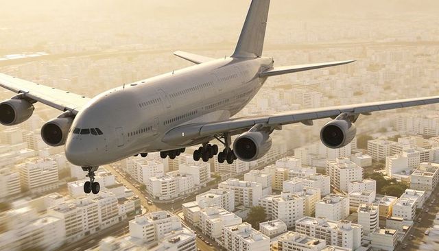 Widebody airliner descending over dense city grid at golden hour with landing gear down