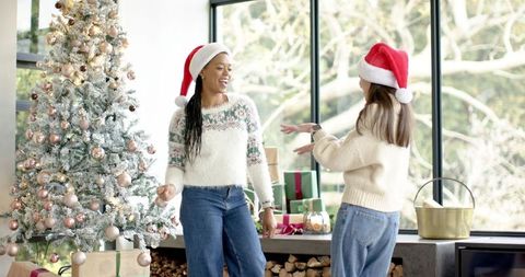 Mixed-race friends wearing santa hats celebrating by flocked christmas tree in cozy home