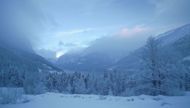 Sunrise breaking through mist over snow-covered boreal forest and frozen mountain lake