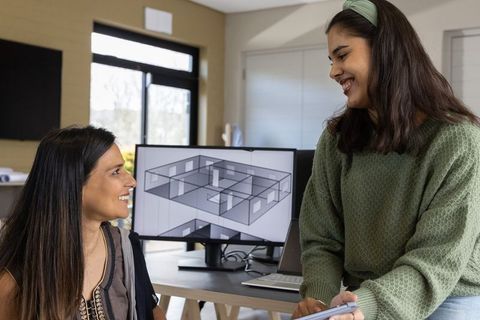 Multicultural women collaborating over 3d floor plan in modern daylight design studio