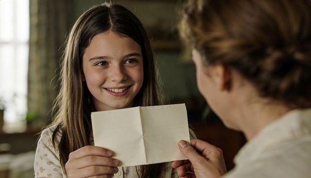 Smiling teen daughter receiving folded note from mother in cozy family home moment