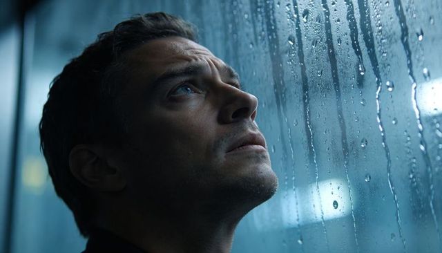 Contemplative man gazing through rain-streaked train window, urban solitude and reflection