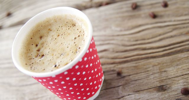 A red polka-dotted paper cup filled with frothy coffee sits on a wooden surface, with copy space - Download Free Stock Photos Pikwizard.com