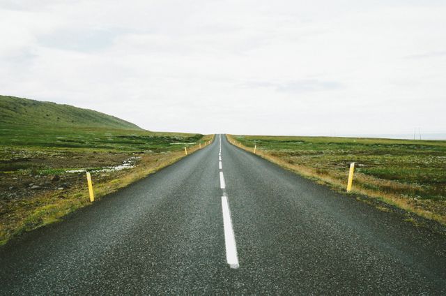 This image shows a long, straight road stretching towards the horizon on a clear day. Ideal for themes such as travel, adventure, solitude, and scenic landscapes. Can be used for travel blogs, website banners, or motivational posters focusing on exploration and journeys.