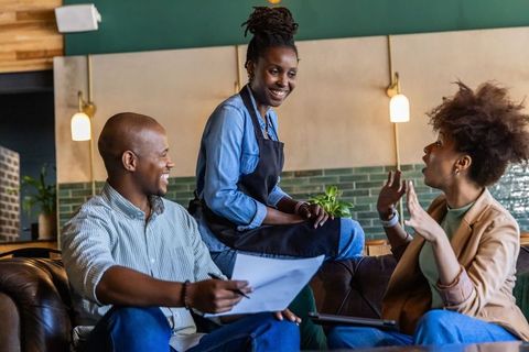 Casual cafe collaboration with barista joining diverse team on sofa discussing plans