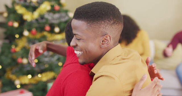 Two happy african american female and male friends hugging at christmas time. christmas festivities, celebrating at home with friends.
