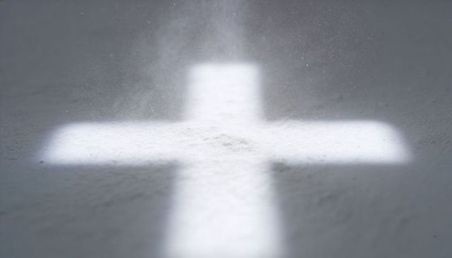 Glowing cross projected onto powdery surface with floating dust, soft monochrome minimal