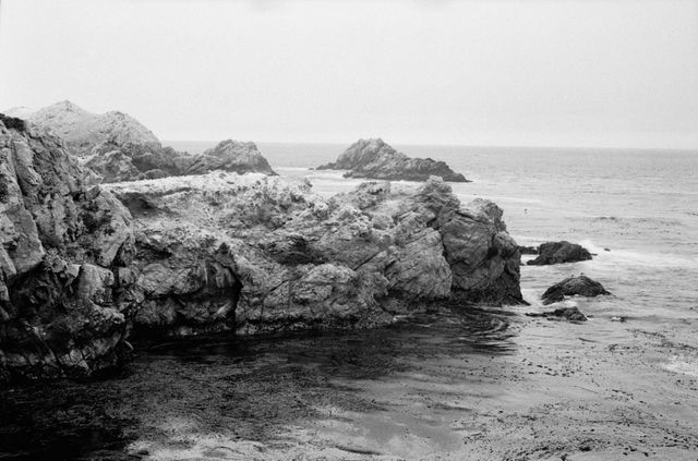 Monochrome depiction of a distant coastal scene with large rocks and gentle ocean waves. Perfect for use in travel brochures, nature and landscape websites, or artwork celebrating the beauty of the natural world. Captures tranquility and evokes a sense of calm and peace.