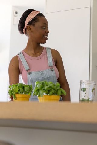 African woman tending basil and blending herbs in minimalist kitchen for home cooking lifestyle