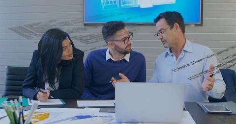 Corporate team collaborating over laptop and blueprints in boardroom meeting